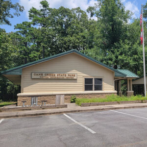 Tan building with American flag on pole and sign saying "Cane Creek State Park Visitor Information Center"