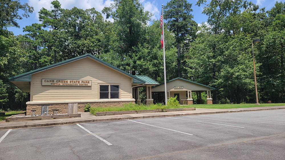 Tan building with American flag on pole and sign saying "Cane Creek State Park Visitor Information Center"