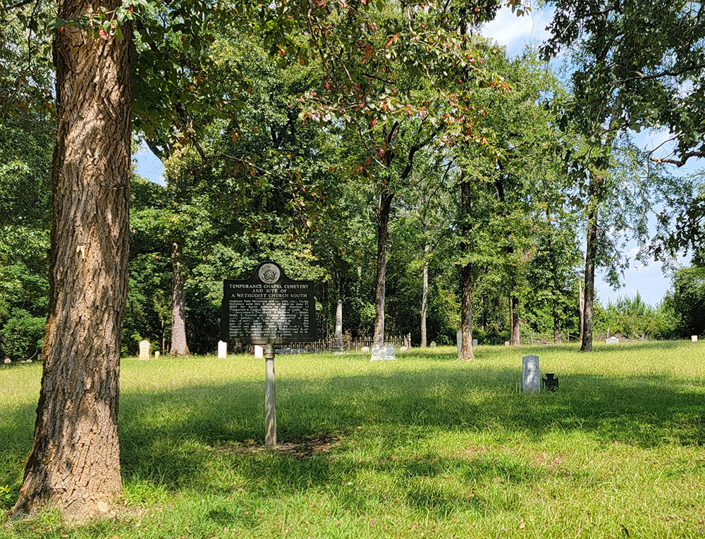 Grassy area with tombstones and an information sign saying "Temperance Chapel Cemetery and site of a Methodist Church South"