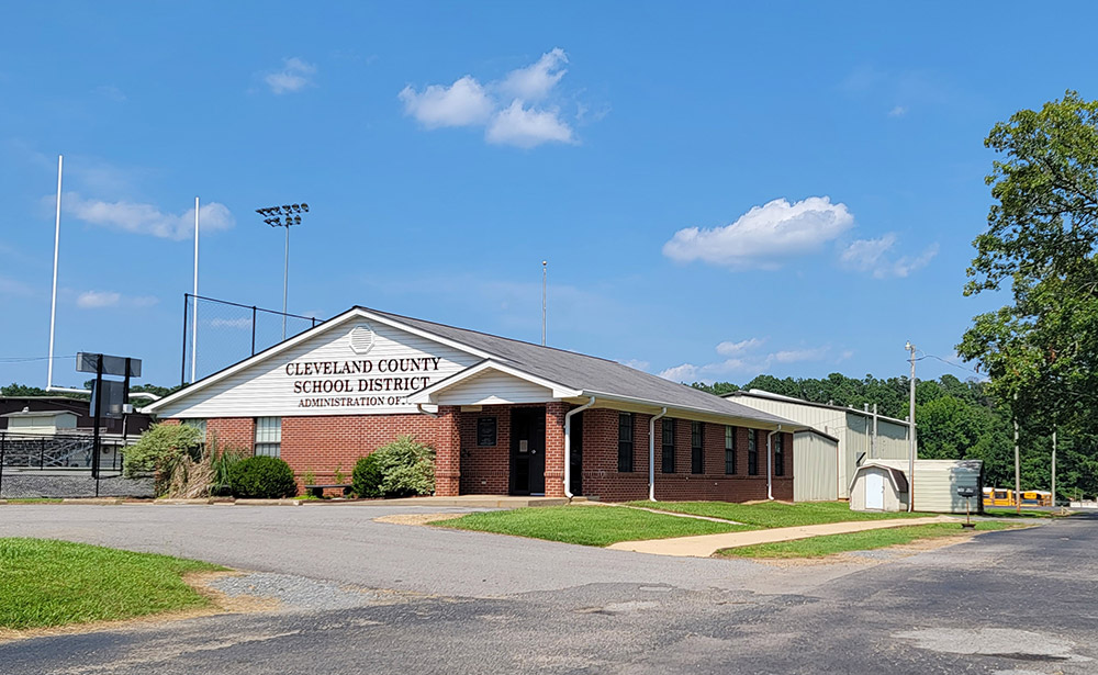 Single-story red brick building with corrugated metal buildings behind it "Cleveland County School District"