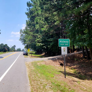 Road running between tall trees with sign "Midway"
