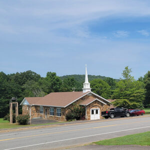 Rock church building with steeple situated by road with trees in background