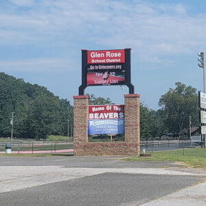 Red sign with white lettering "Glen Rose School District Home of the Beavers" and parking lot
