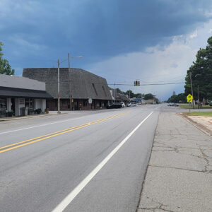 Small town street with storefront buildings on the left and parking lot on the right