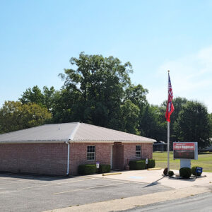 Single story red brick building with flags on flagpole and parking lot