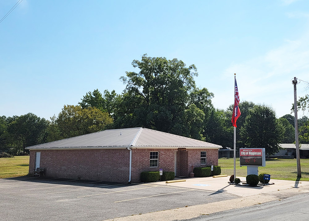 Single story red brick building with flags on flagpole and parking lot