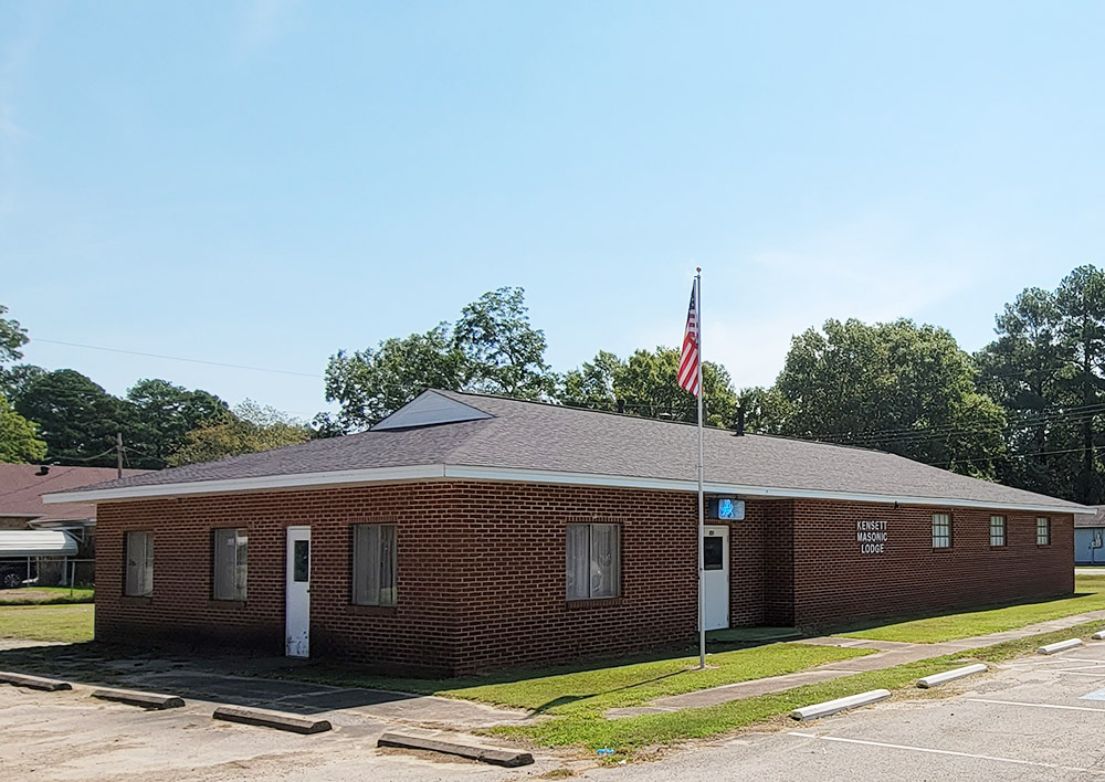 Single story red brick building with American flag on pole "Kensett Masonic Lodge" and parking lot