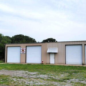 Single story tan metal building with four garage doors and one entrance door