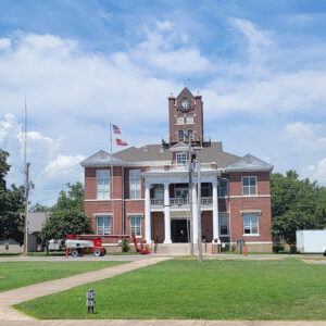 Multistory red brick building with clock tower and white columns with construction equipment in front