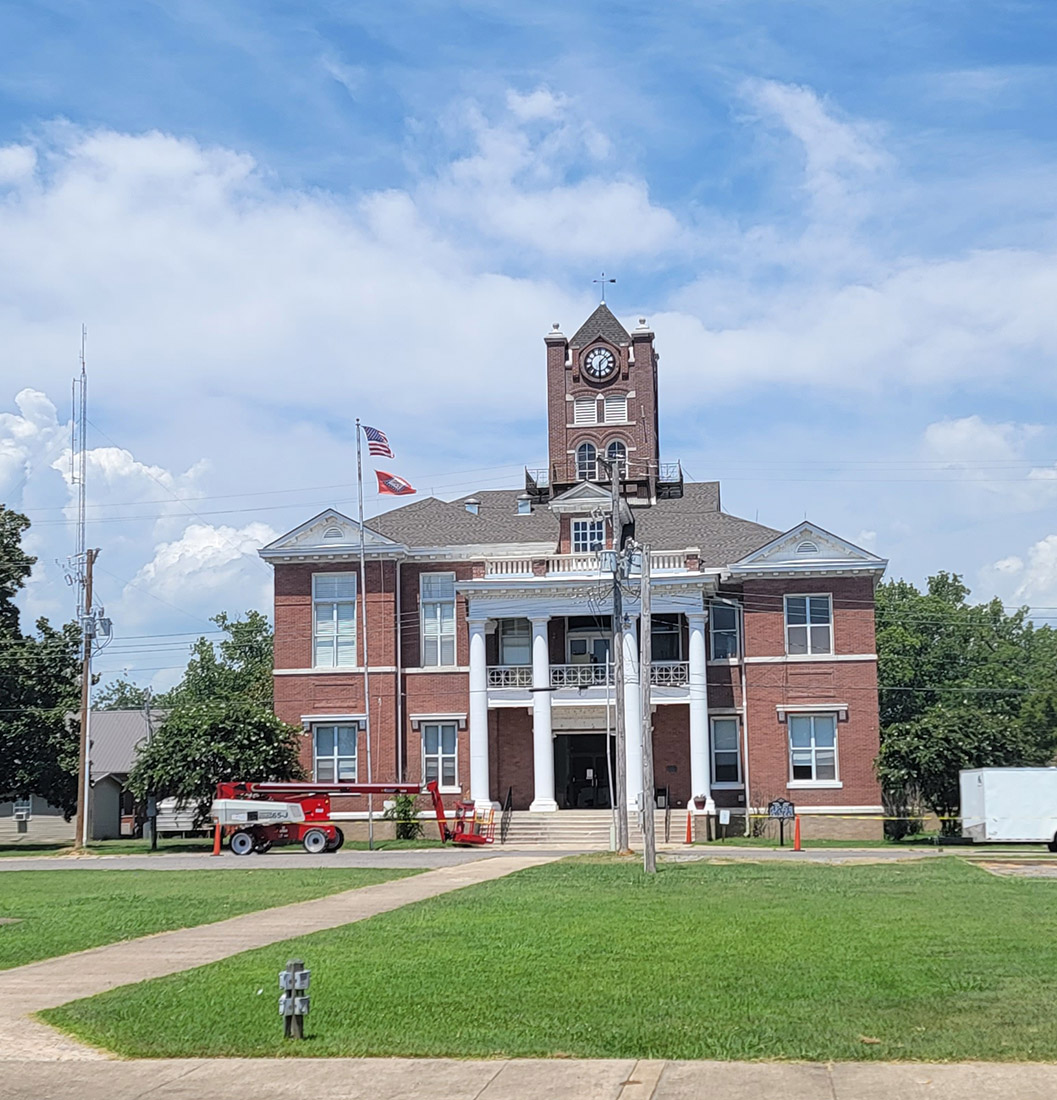 Multistory red brick building with clock tower and white columns with construction equipment in front