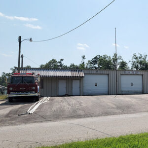 Single story gray metal building with doors and three bays and a red fire truck sitting out front