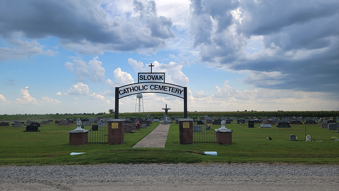 Cemetery with grass and gravestones and arched sign reading "Slovak Catholic Cemetery"