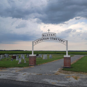 Cemetery with grass and gravestones and arched sign reading "Slovak Lutheran Cemetery"