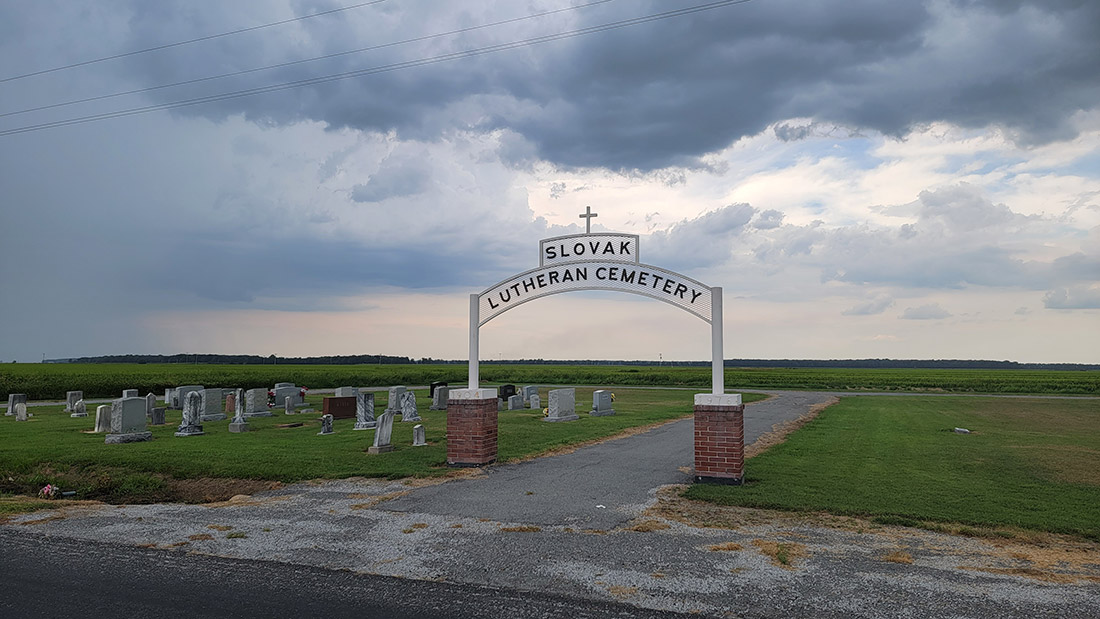 Cemetery with grass and gravestones and arched sign reading "Slovak Lutheran Cemetery"