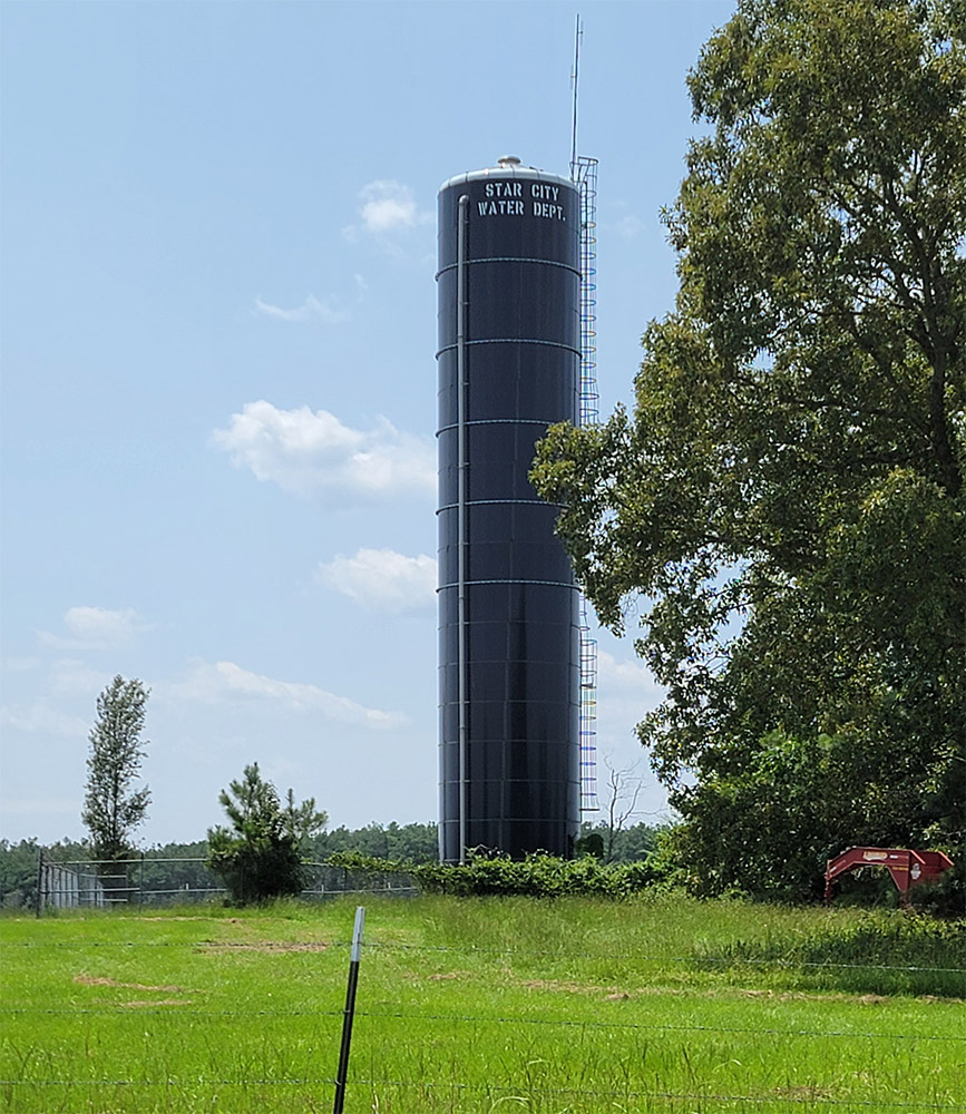 Large black cylindrical tower in the middle of a field with "Star City Water Department" on it in white letters