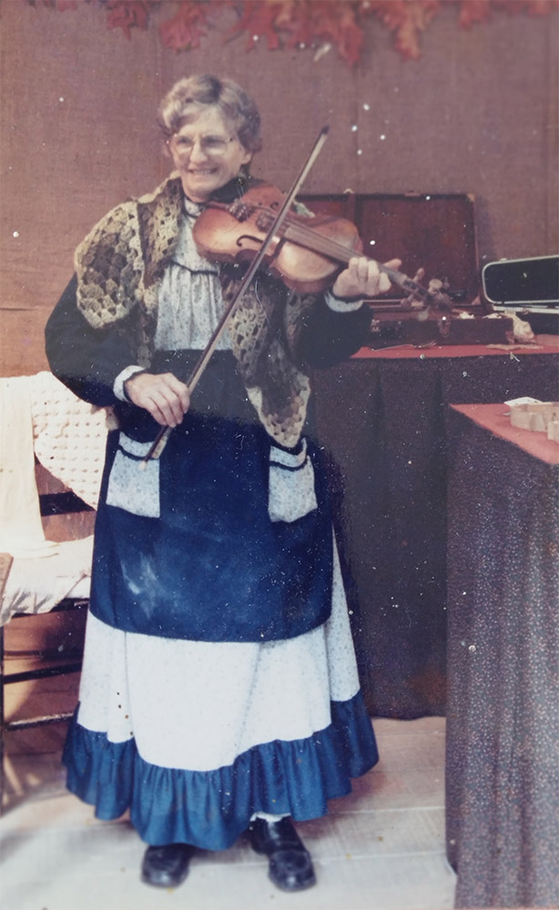 Older white woman wearing dress and playing fiddle