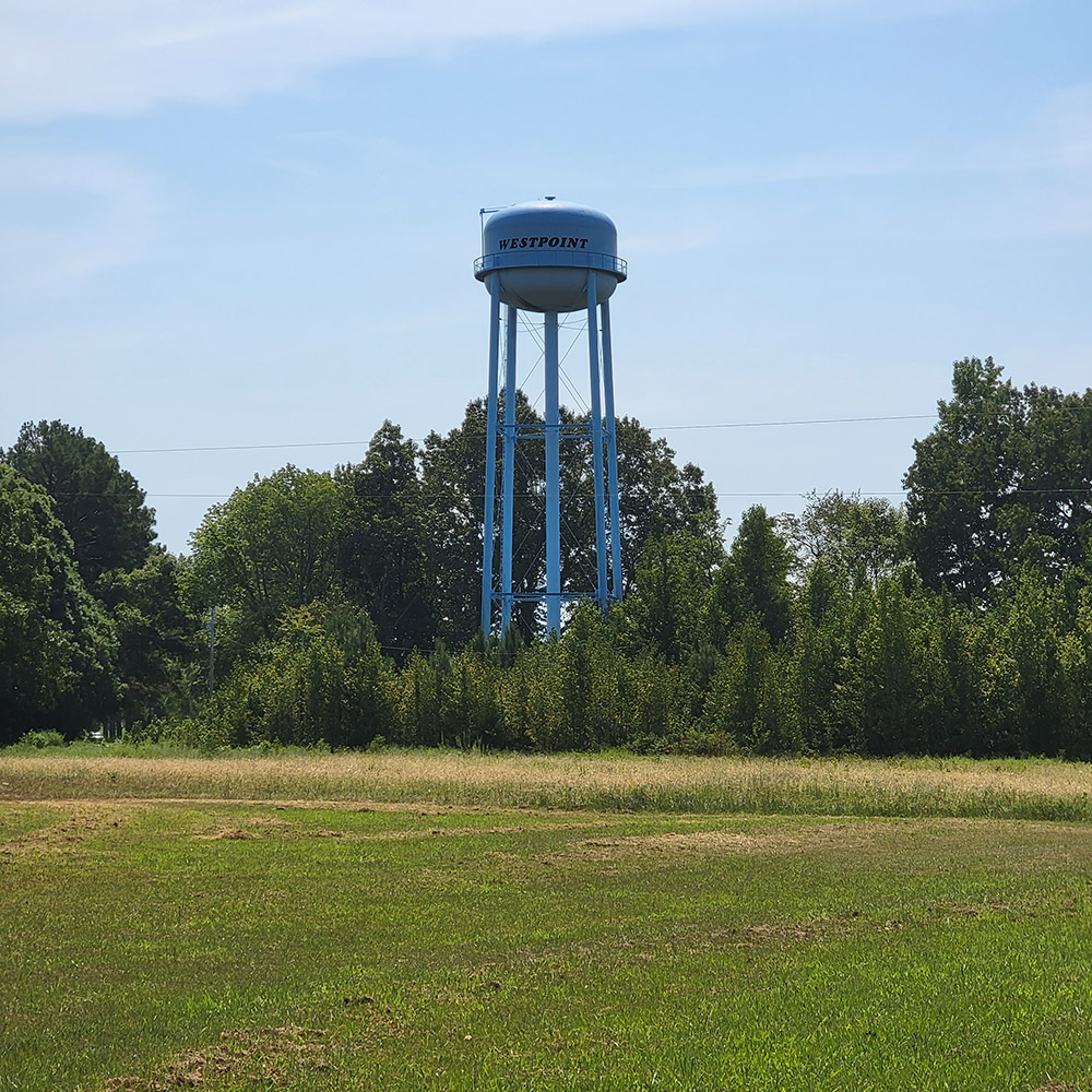 blue water tower with "West Point" printed on it standing amid trees