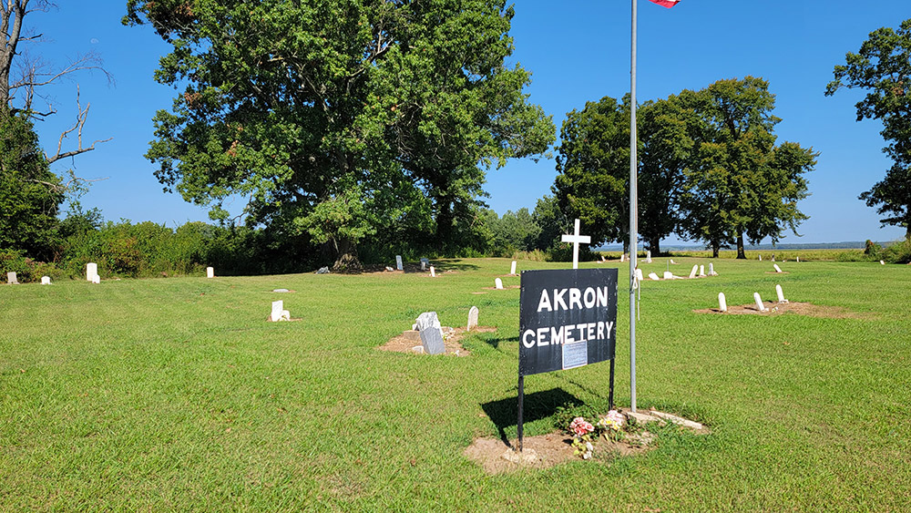 gravestones on green grass and sign saying "Akron Cemetery" and trees in background