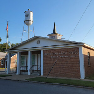 Single story red brick post office building with water tower in background