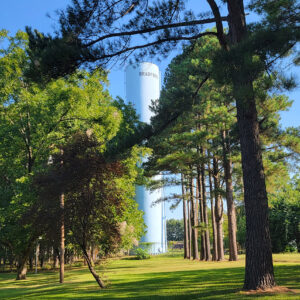 Tall white cylinder water tower with "Bradford" printed on it with trees in foreground
