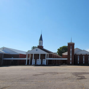 Multistory red brick church building with white columns in front and a steeple and massive parking lot