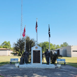 Veterans memorial with names on it with two statues of soldiers and three flags