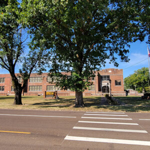 Multistory rectangular red brick school building with trees and road with crosswalk