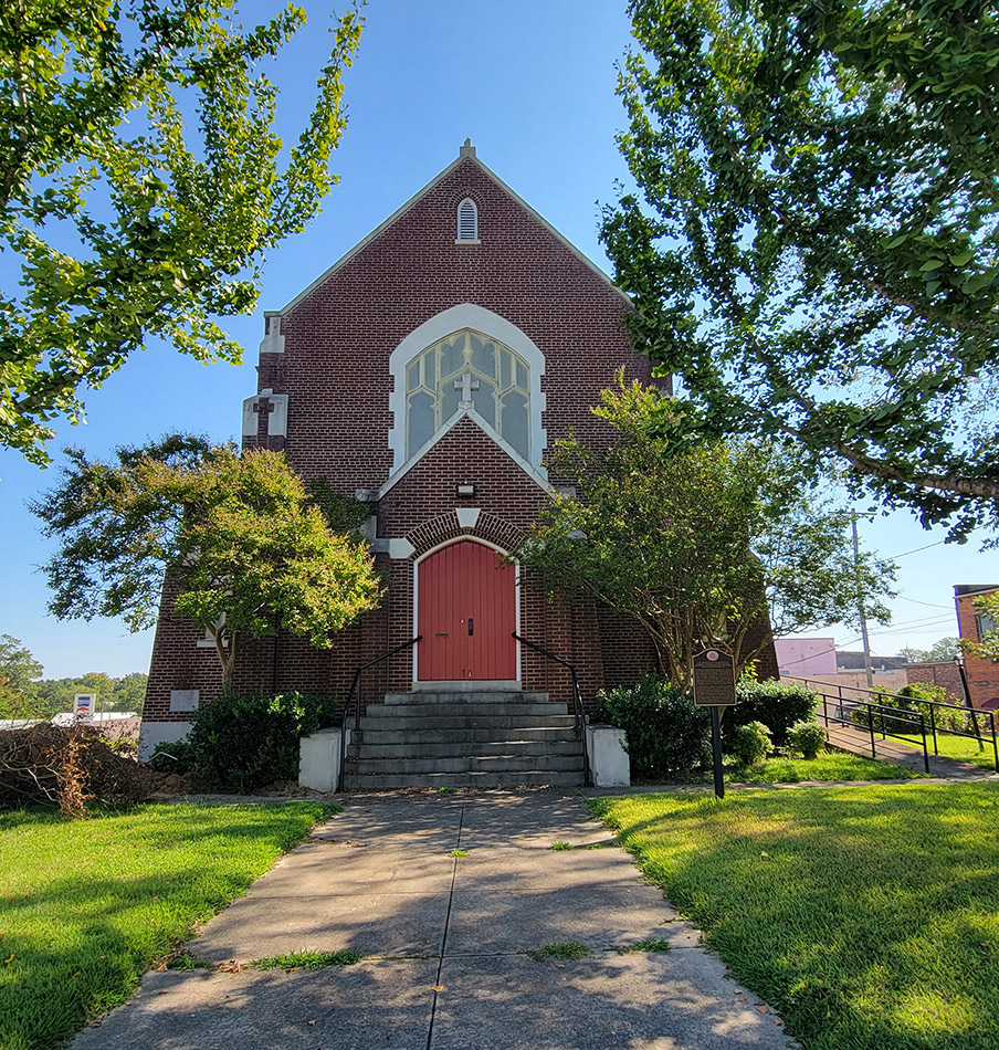Multistory red brick church building with steps leading up to red doors