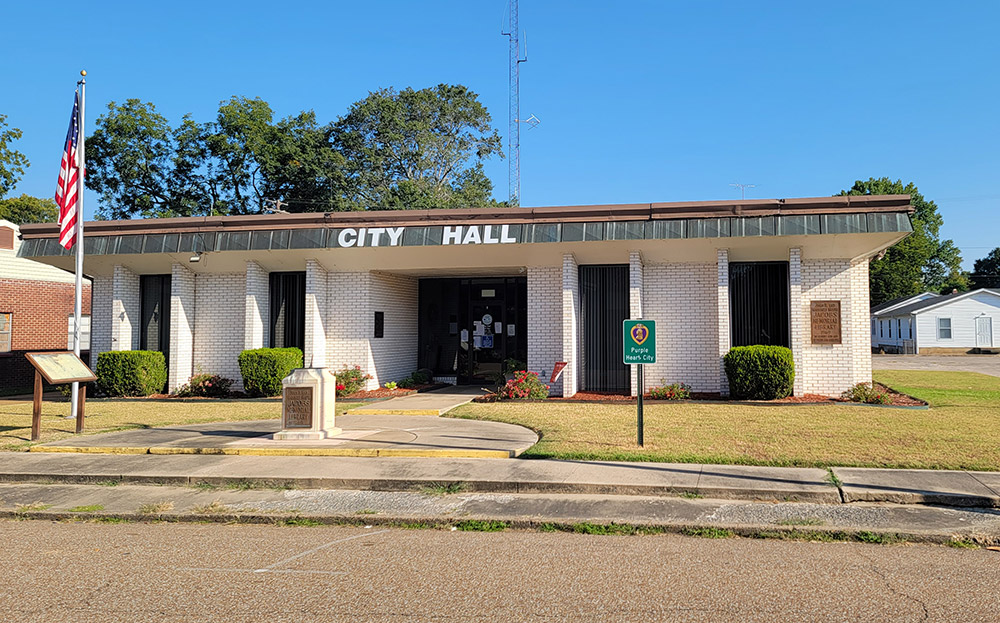 Single story white brick building with "City Hall" appearing in large white letters across the front