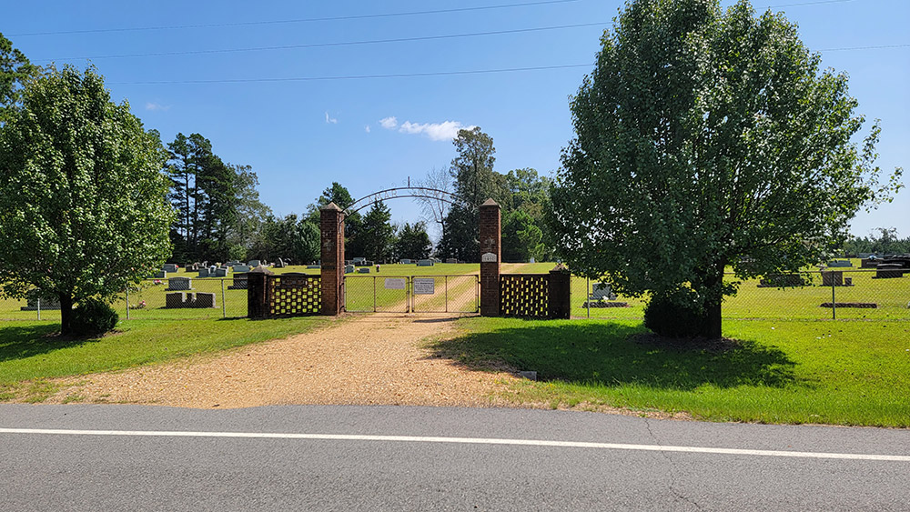 Brick arched gate leading into cemetery with tombstones and trees