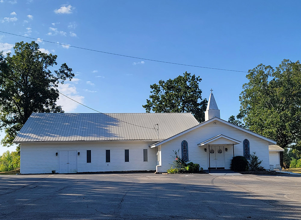 white wooden church building with steeple and parking lot