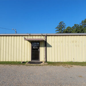 Single story yellow metal building with gravel lot