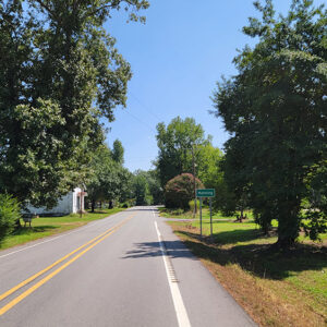 Rural road with scattered trees and houses and sign saying "Manning"