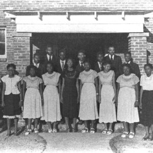 African American boys and girls in suits and dresses standing in front of a brick building