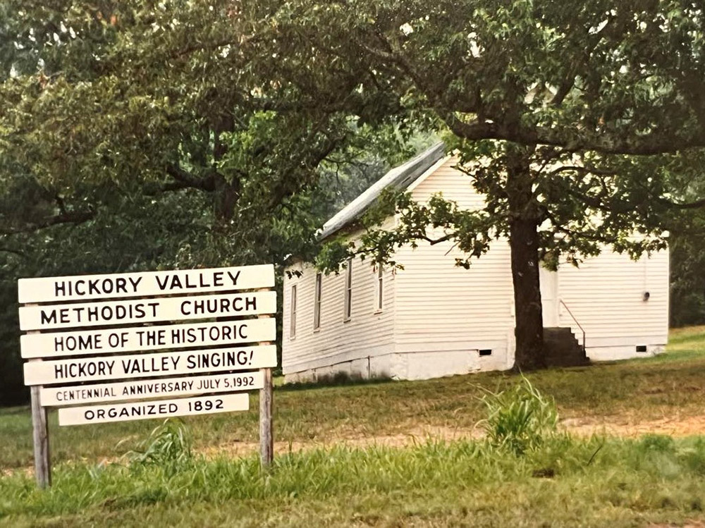 Single story white wooden church building and sign saying "Home of the Historic Valley Singing"