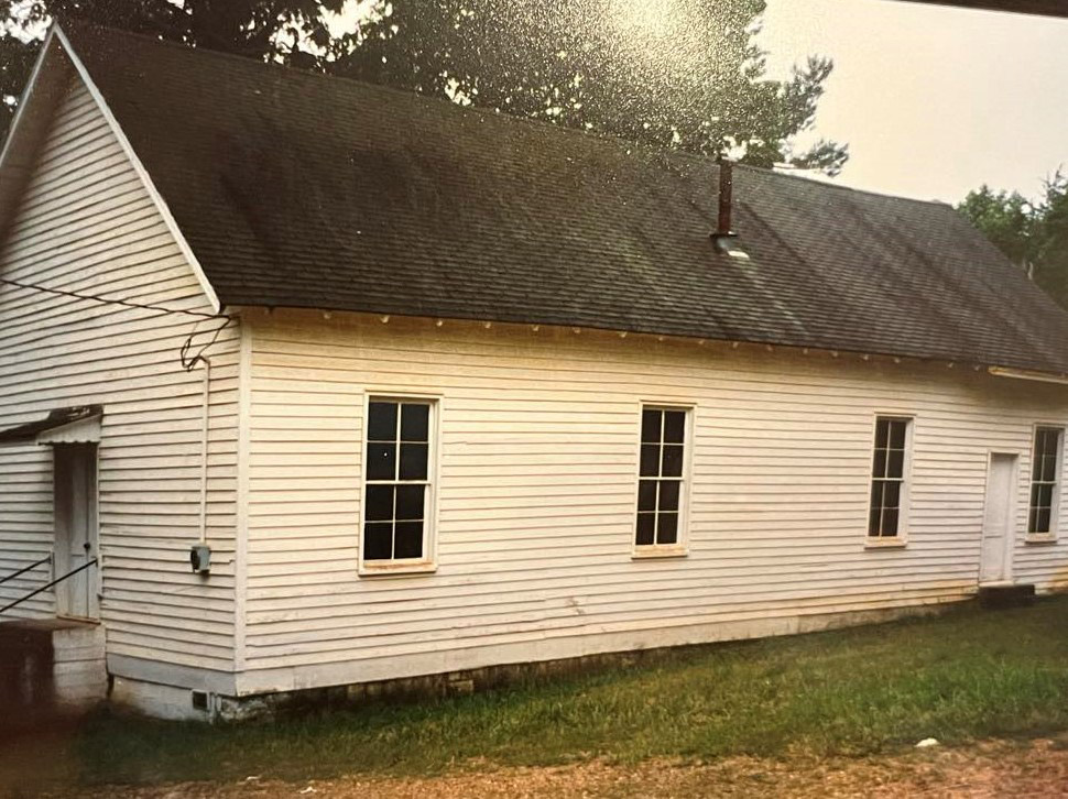 Single story white wooden church building with windows along the side