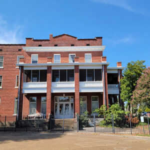 Multistory red brick building with a white upper balcony