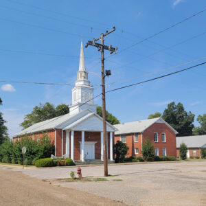 Multistory red brick church building with white columns and a white steeple and parking lot