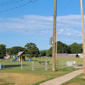 Fenced in area containing children's playground equipment with trees in background