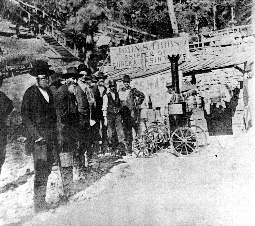 Men gathered by sign saying "John S. Tibbs Shipper of Eureka Basin Water" in front of steep staircase up hill