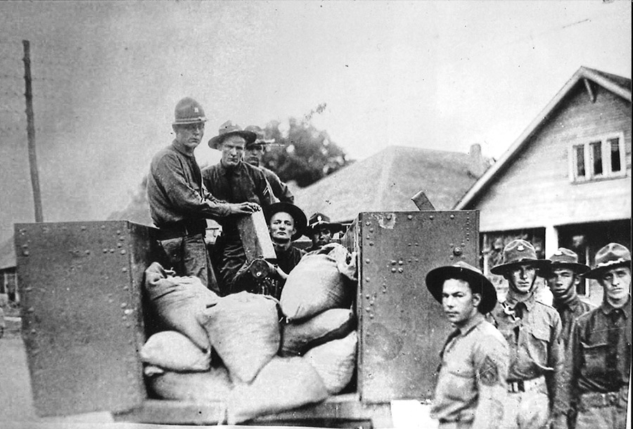 White men in military garb sitting in and standing around a truck loaded with bags