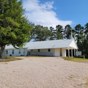White wooden church building with steeple and gravel parking lot
