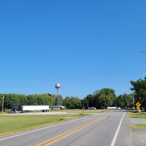 Highway entering small town past some semi trucks and a water tower