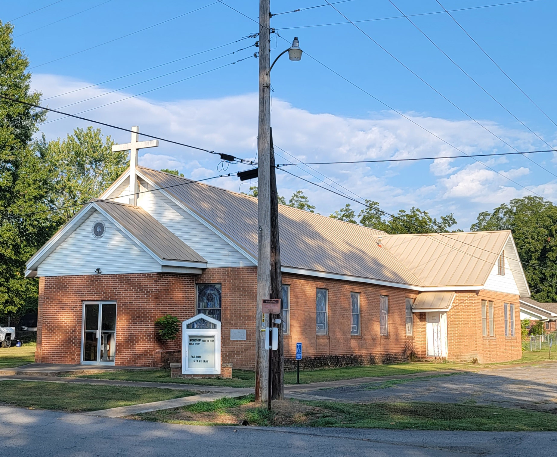 Orange-red brick church building with stained glass windows and parking lot