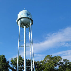 white water tower with "Russell" on it in blue behind buildings