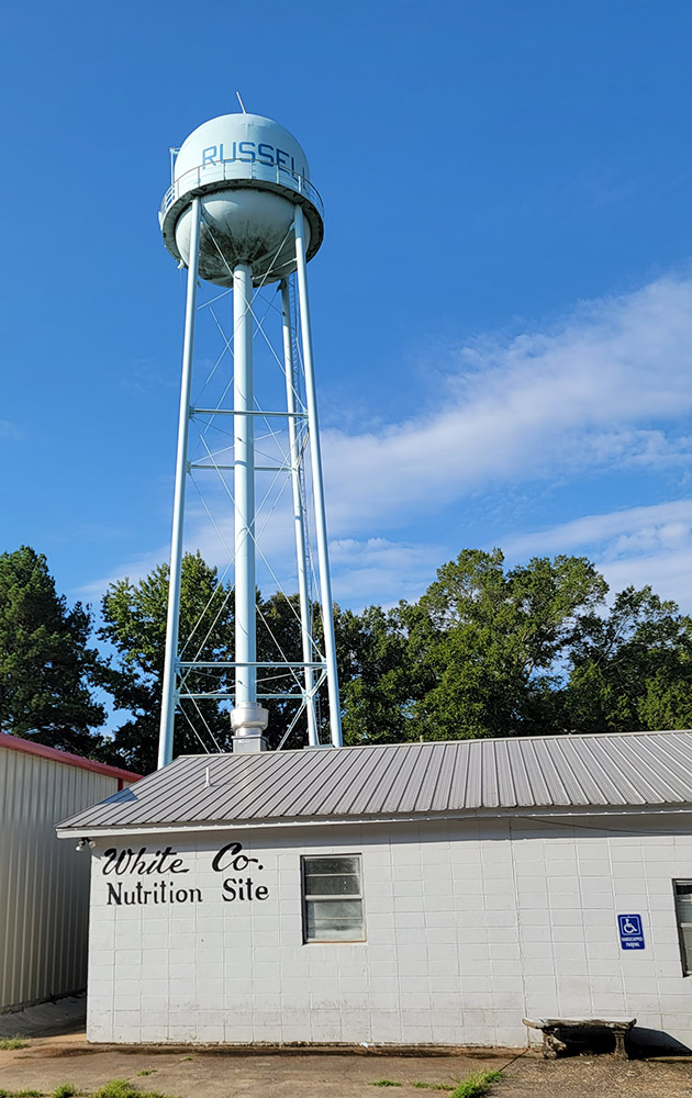 white water tower with "Russell" on it in blue behind buildings