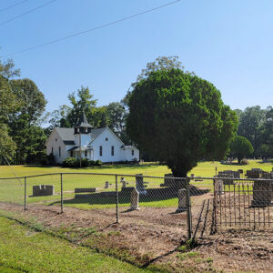 White country church building with bell tower in distance with cemetery and trees in foreground