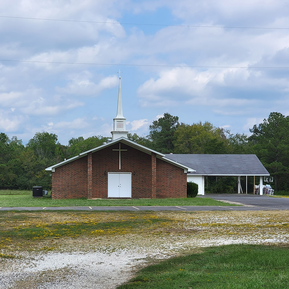 Red brick church building with steeple and parking lot and covered side entrance