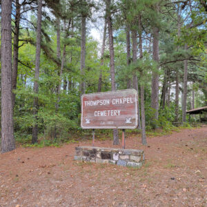 Wooden sign among conifer trees with sign saying "Thompson Chapel Cemetery"