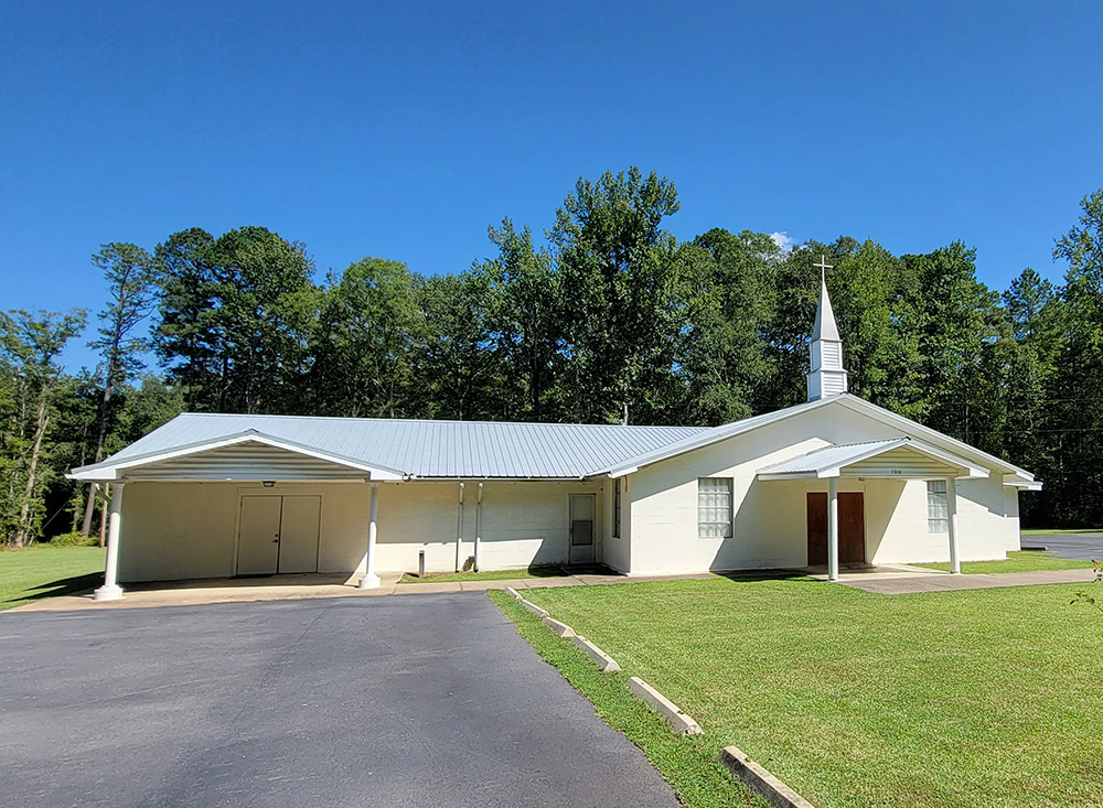 Single story white concrete block church building with steeple and covered front and side entrances